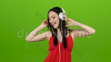 女孩通过耳机听欢<strong>快</strong>而<strong>充</strong>满活力的音乐。 绿色屏幕